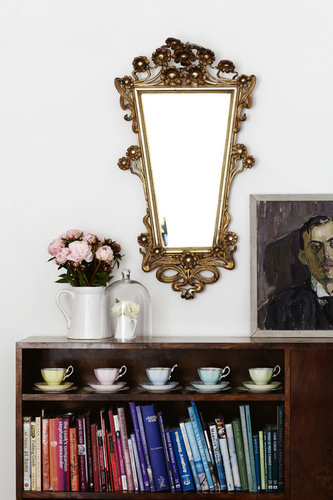 espejo y cerámica antigua con librería nórdica y libros ordenados cromáticamente / old mirronr and china with a nordic library and books cromatically displayed