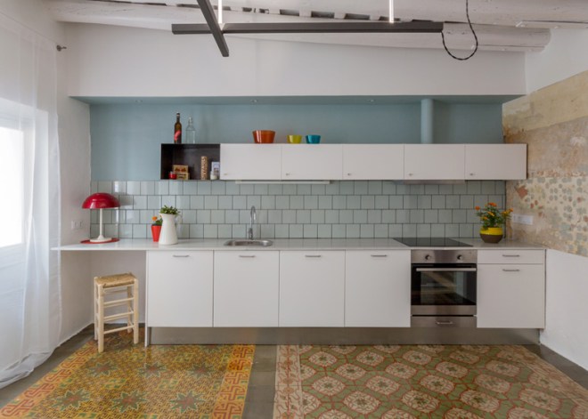 Continuando con la misma gama de color, la cocina se alicata de azulejo gris azulado. Los muebles son blancos; se repite la colocación de una caja a modo de estante.