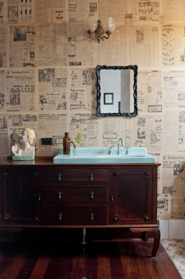 En el baño han reciclado un aparador antiguo como mueble de lavabo. Me gusta el efecto que hace el papel de periódico con el espejo.