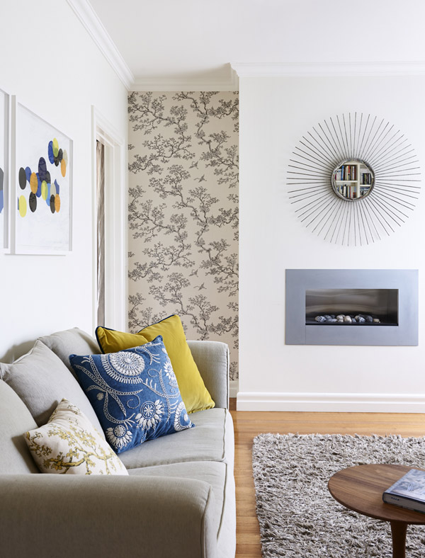 Zona de estar con un maravilloso espejo de sol, una chimenea encastrada en la pared y un papel pintado en la esquina que da su toque a este espacio de elementos sobrios.