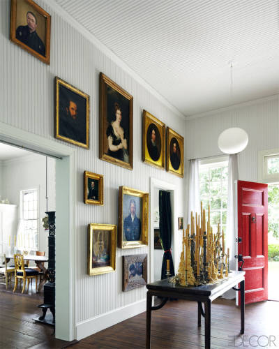 En la entrada de la vivienda se ha dispuesto una composición de pinturas de diferentes estilos, con marcos dorados que resaltan frente a la pared blanca.