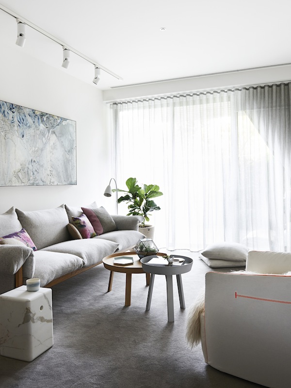 La zona de estar con el sofá de estructura de madera y demás elementos blancos dan protagonismo al cuadro que se encuentra encima del sofá.