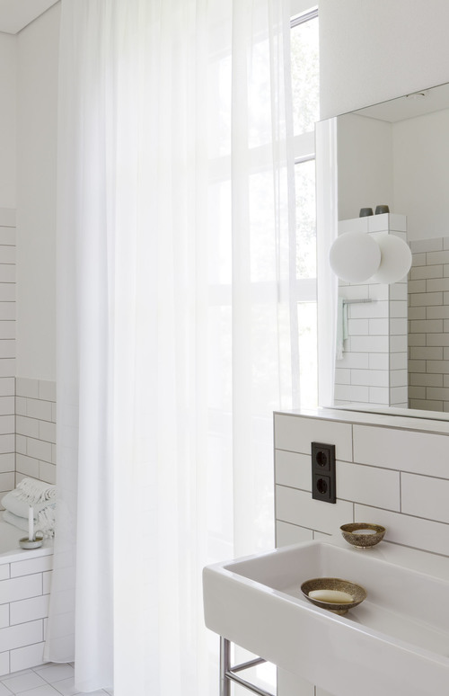 Las baldosas blancas rectangulares del baño, la junta negra y los apliques de globo dan a este baño un aire retro precioso.